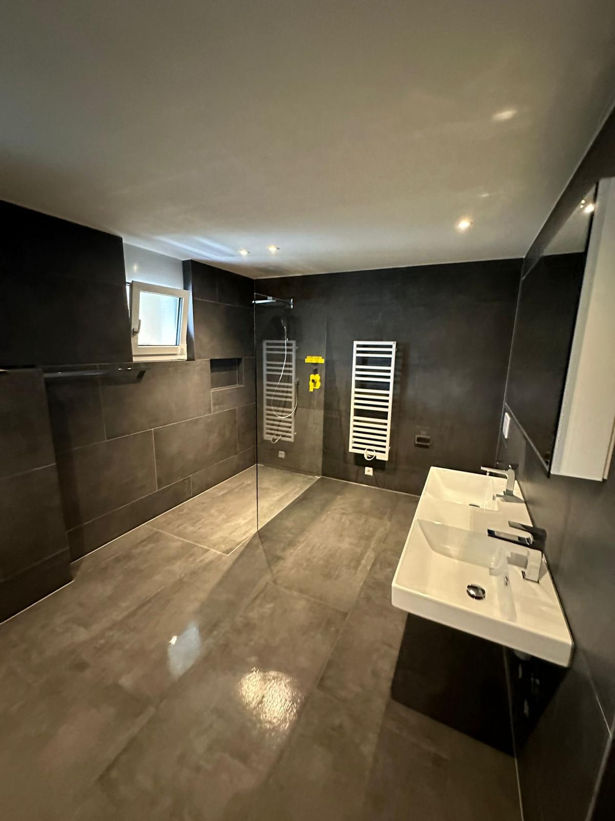 Modernes Badezimmer mit dunklen Platten und glänzendem Boden